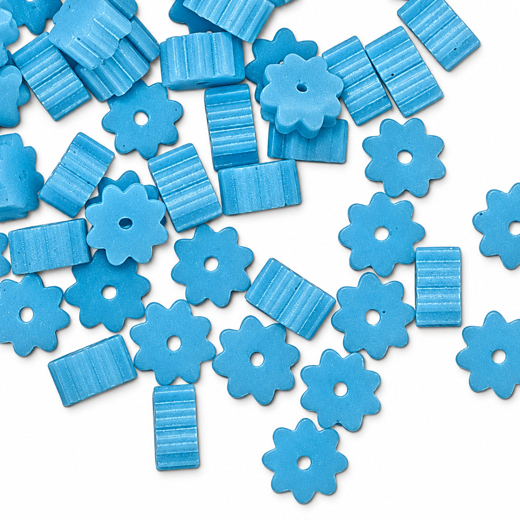 Light blue flower-shaped and rectangular beads with horizontal ridges scattered on a white background.