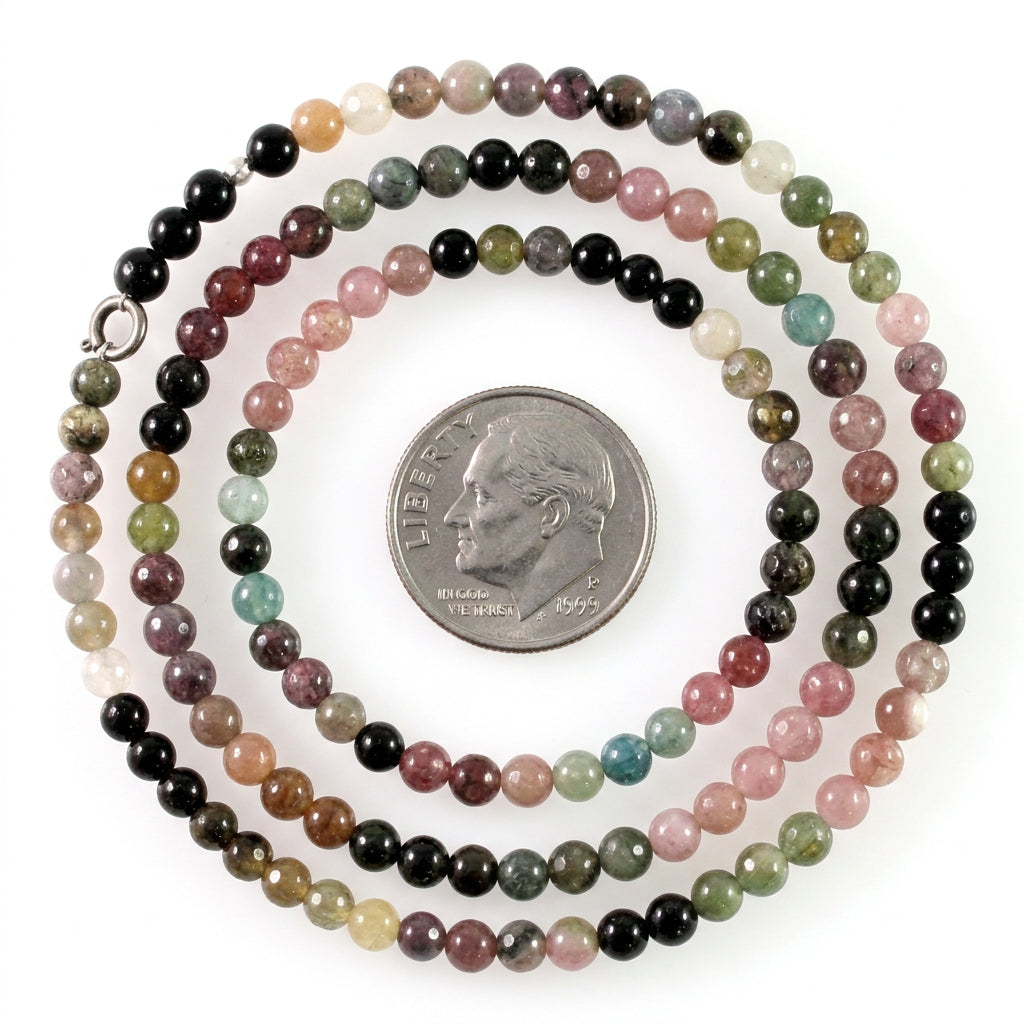 A beaded strand necklace made of small polished round beads in multiple colors including black, pink, green, brown, and white, shown with a silver coin for scale on a white background.