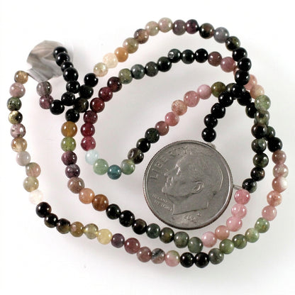 A multi-strand beaded necklace made of polished round gemstone beads in various colors, including pink, green, black, brown, and white, shown with a US quarter coin for scale on a white background.