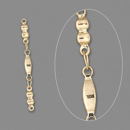 Gold chain link detail showing a close-up of a section with a small oval tag, on a solid gray background.