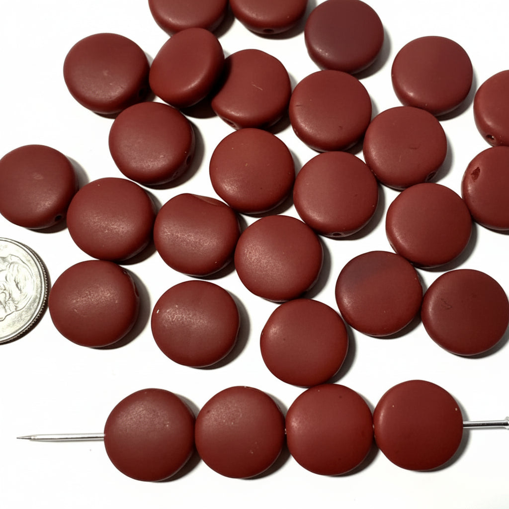 A group of round, dark reddish-brown beads scattered on a white surface, with a coin and a sewing pin used for scale.