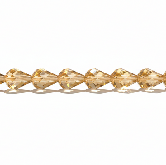 A strand of faceted, teardrop-shaped crystal beads in a warm golden-yellow color, arranged horizontally on a clean white background.