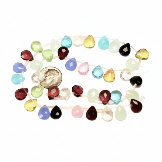 A strand of faceted teardrop-shaped gemstone beads in assorted colors, including red, blue, green, yellow, pink, black, and clear, arranged in a loose circle on a white background with a small gold coin for scale.