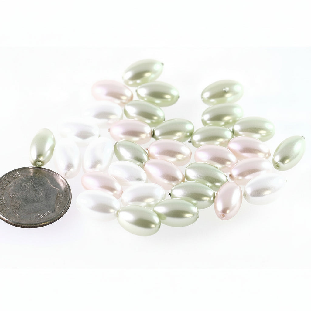 A group of small oval pearl-like beads in soft pastel shades of pale green, blush pink, and white, arranged on a white background with a coin for scale.