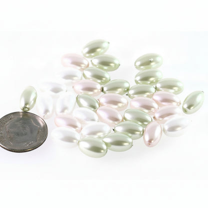 A group of small oval pearl-like beads in soft pastel shades of pale green, blush pink, and white, arranged on a white background with a coin for scale.