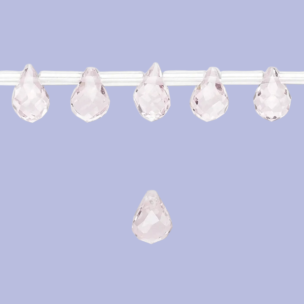 Five faceted teardrop-shaped clear rhinestones or crystal beads strung horizontally on a thin white cord, with one matching crystal bead floating below against a solid light periwinkle background.