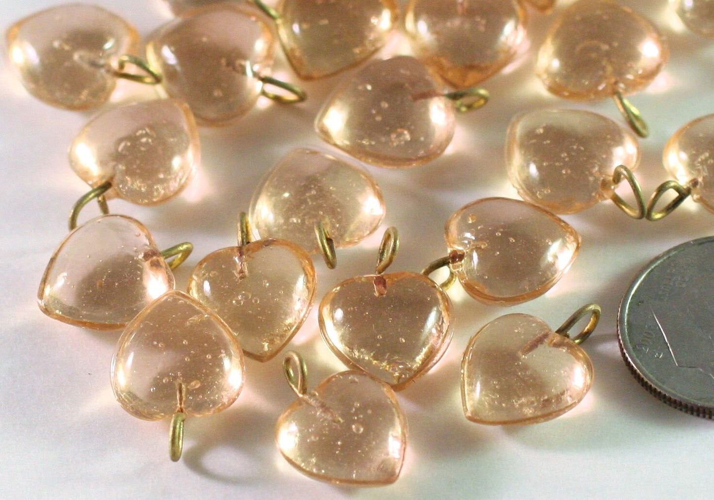 Heart-shaped peach beads with gold wire on a white background, next to a coin for scale.