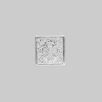 A square silver-toned metal charm with an embossed floral filigree pattern, centered on a solid gray background.