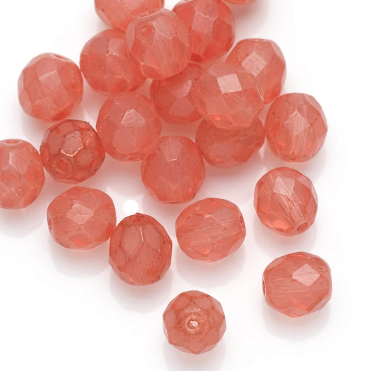 Faceted round beads in a translucent coral pink color scattered on a plain white background.