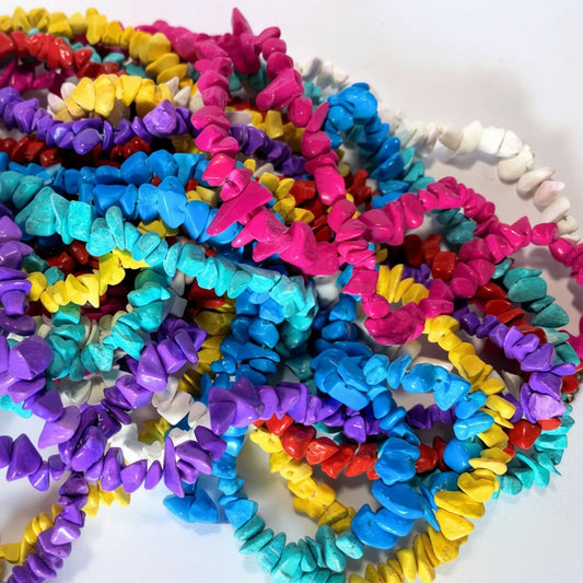 A pile of colorful chip-style beads in multiple strands, including pink, blue, turquoise, purple, yellow, red, and white, photographed on a plain light background.