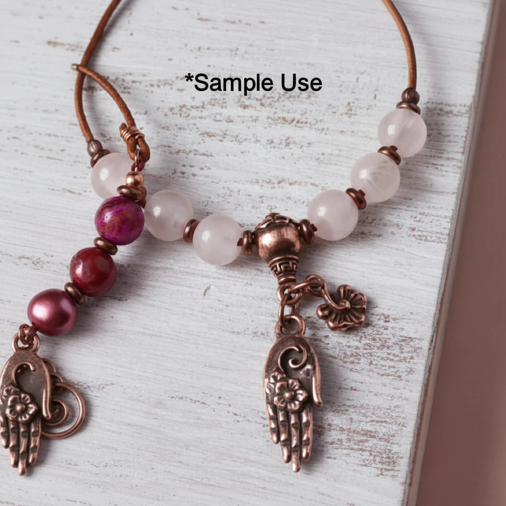 A close-up of a beaded necklace with translucent pale pink beads, a copper-toned central bead, a dangling hand-shaped charm with floral details, and a small flower charm, laid on a distressed white wood surface. Black text at the top reads '*Sample Use'.