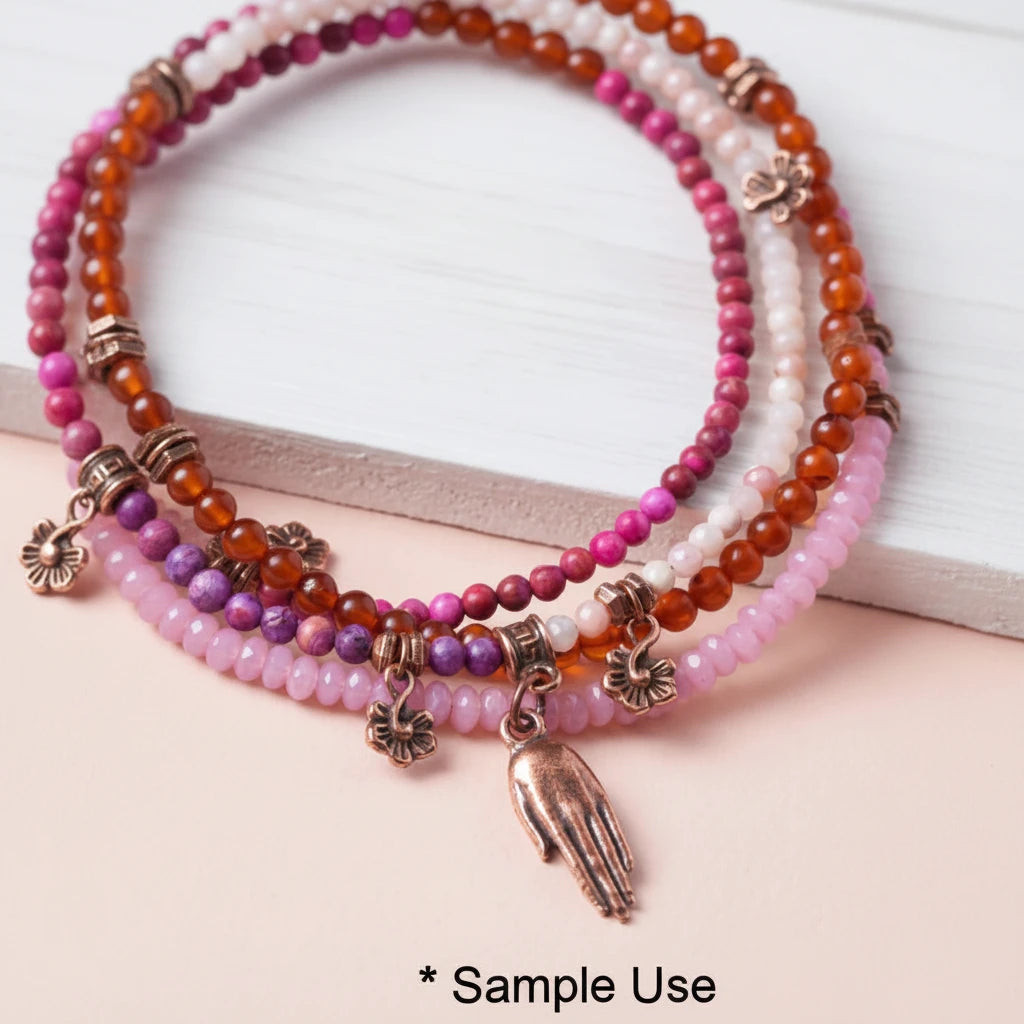 A close-up of a multi-strand beaded bracelet set with pink, purple, orange, and white beads, bronze-toned flower charms, and a bronze hand pendant, displayed on a light pink surface with a white block in the background. The text '* Sample Use' is visible at the bottom.