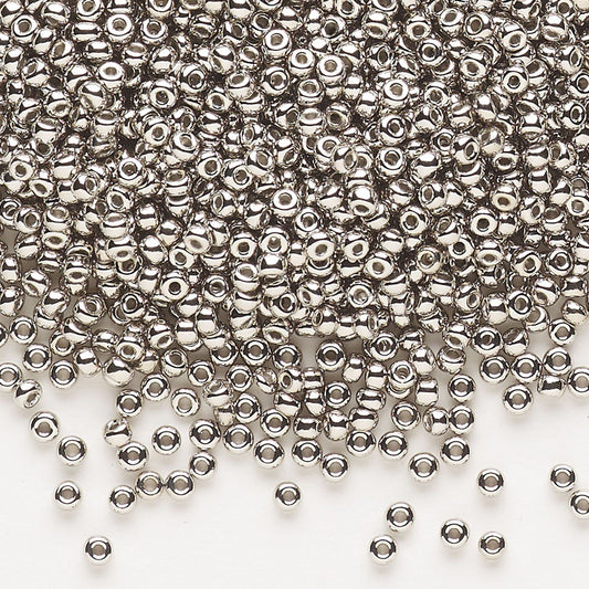 A pile of small metallic silver seed beads with a central hole, scattered across a plain white background.
