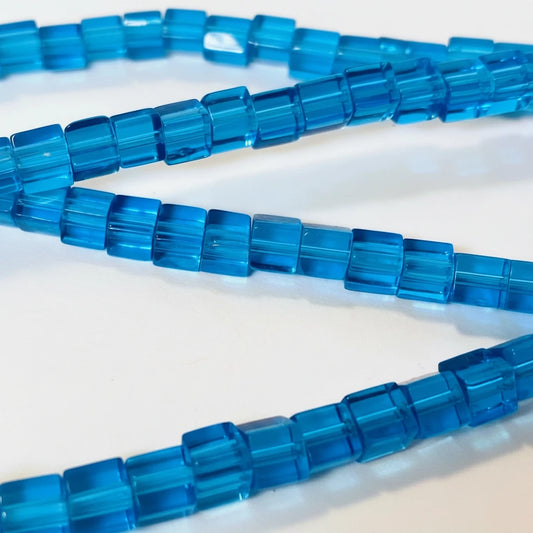 Blue translucent rectangular faceted beads strung on a cord, shown in a close-up view against a white background.