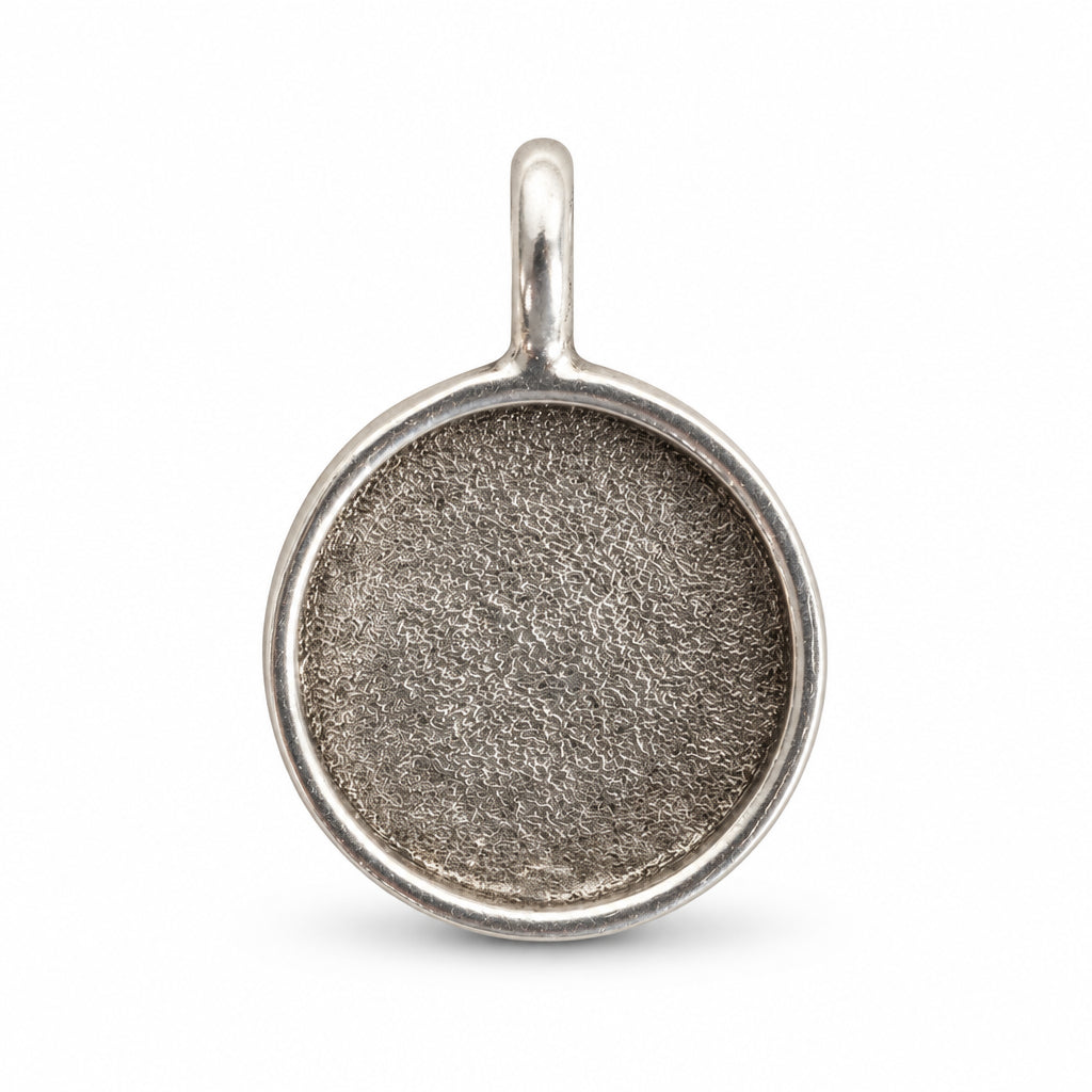 A round silver pendant or charm blank with a textured center and a small top loop, shown on a plain white background.