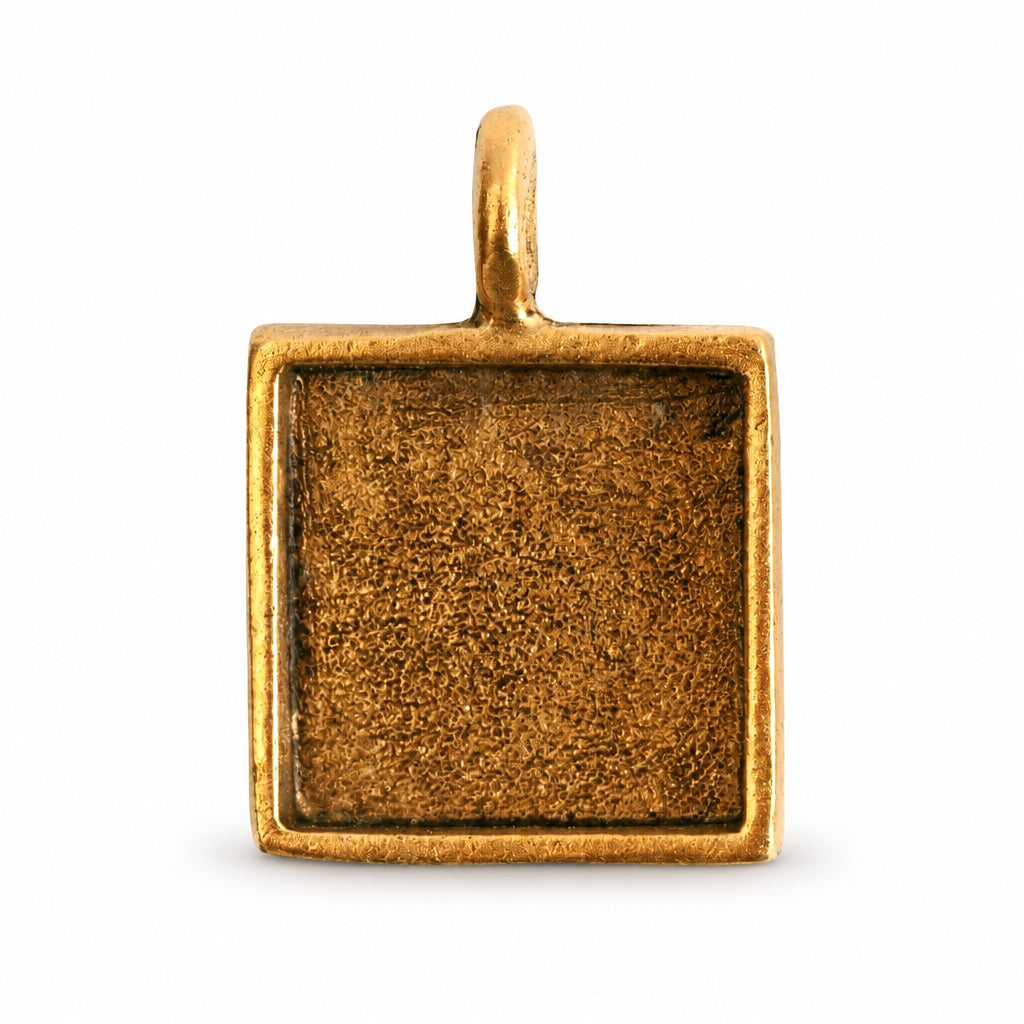 A square gold-toned metal pendant or charm blank with a textured center recess and a small top loop, shown on a plain white background.