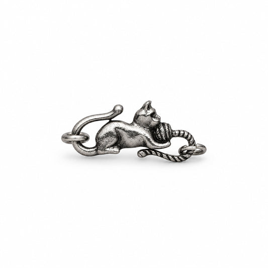 A silver-toned metal charm shaped like a lying cat holding a ball of yarn, photographed on a plain white background.