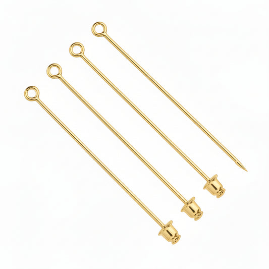 Four gold metal cocktail picks with looped ends and tapered tips, arranged diagonally on a plain white background.