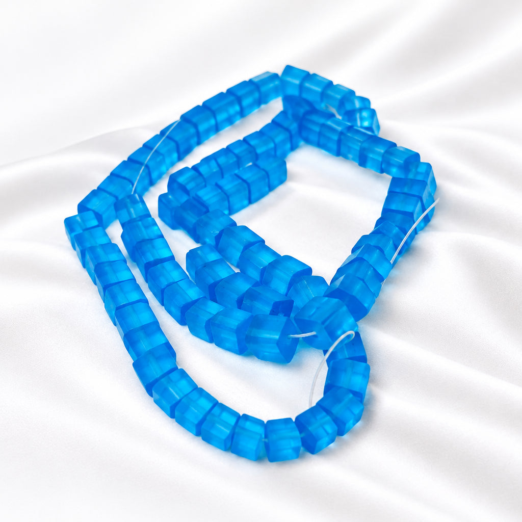 A close-up of translucent blue faceted beads strung on a clear cord, arranged on a plain white background.
