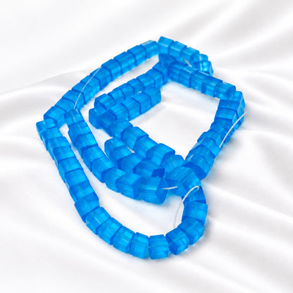 A close-up of translucent blue faceted beads strung on a clear cord, arranged on a plain white background.