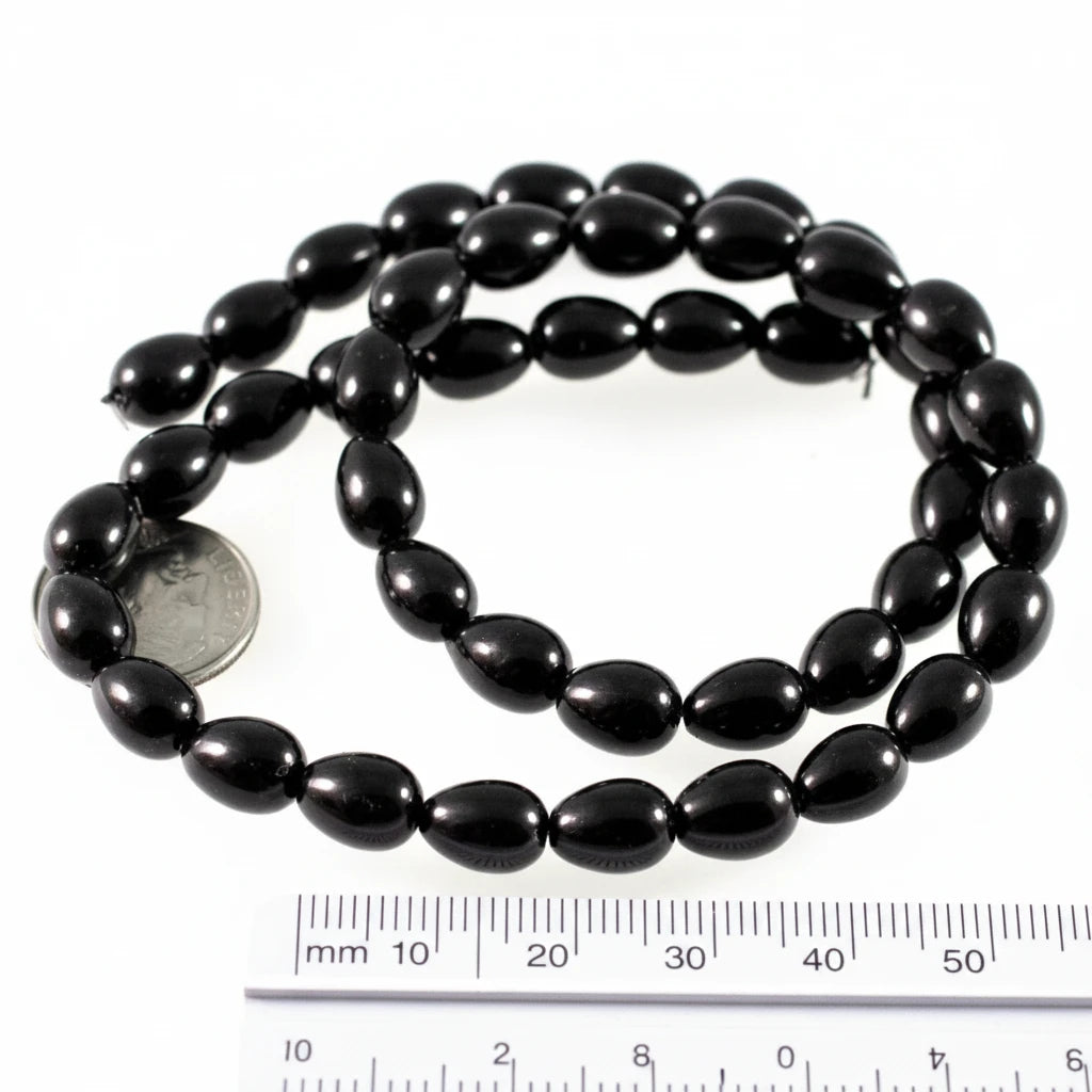 A strand of glossy black oval beads coiled on a white background, with a US quarter coin and a 50 mm ruler included for scale.