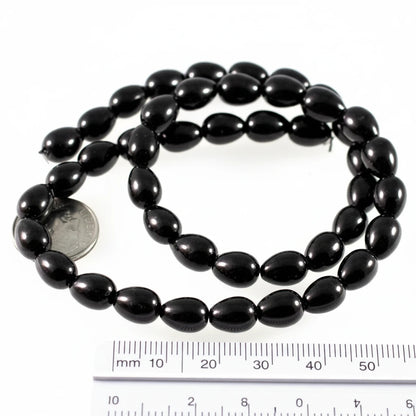 A strand of glossy black oval beads coiled on a white background, with a US quarter coin and a 50 mm ruler included for scale.