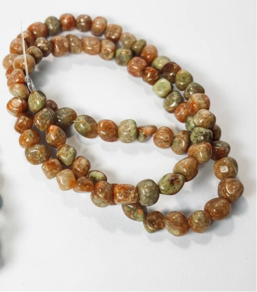 A strand of polished tumbled gemstone beads in earthy brown, orange, and green marbled patterns, coiled on a white background.