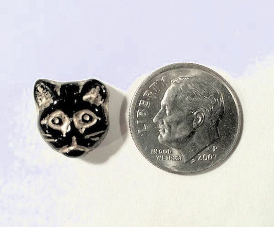 Small silver cat-shaped object next to a dime coin on a white background