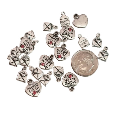 A set of silver-toned metal charms for jewelry making, featuring heart and envelope designs with 'Made with Love' engravings and a small red heart accent, displayed on a white background next to a US quarter for scale. The text 'The Mystical Garden Path' is visible at the bottom.