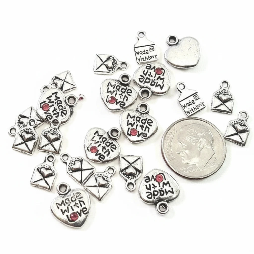 Silver-toned metal charms for jewelry making, including heart-shaped pendants with 'Made with Love' and envelope charms, arranged on a white background with a US dime for scale reference.