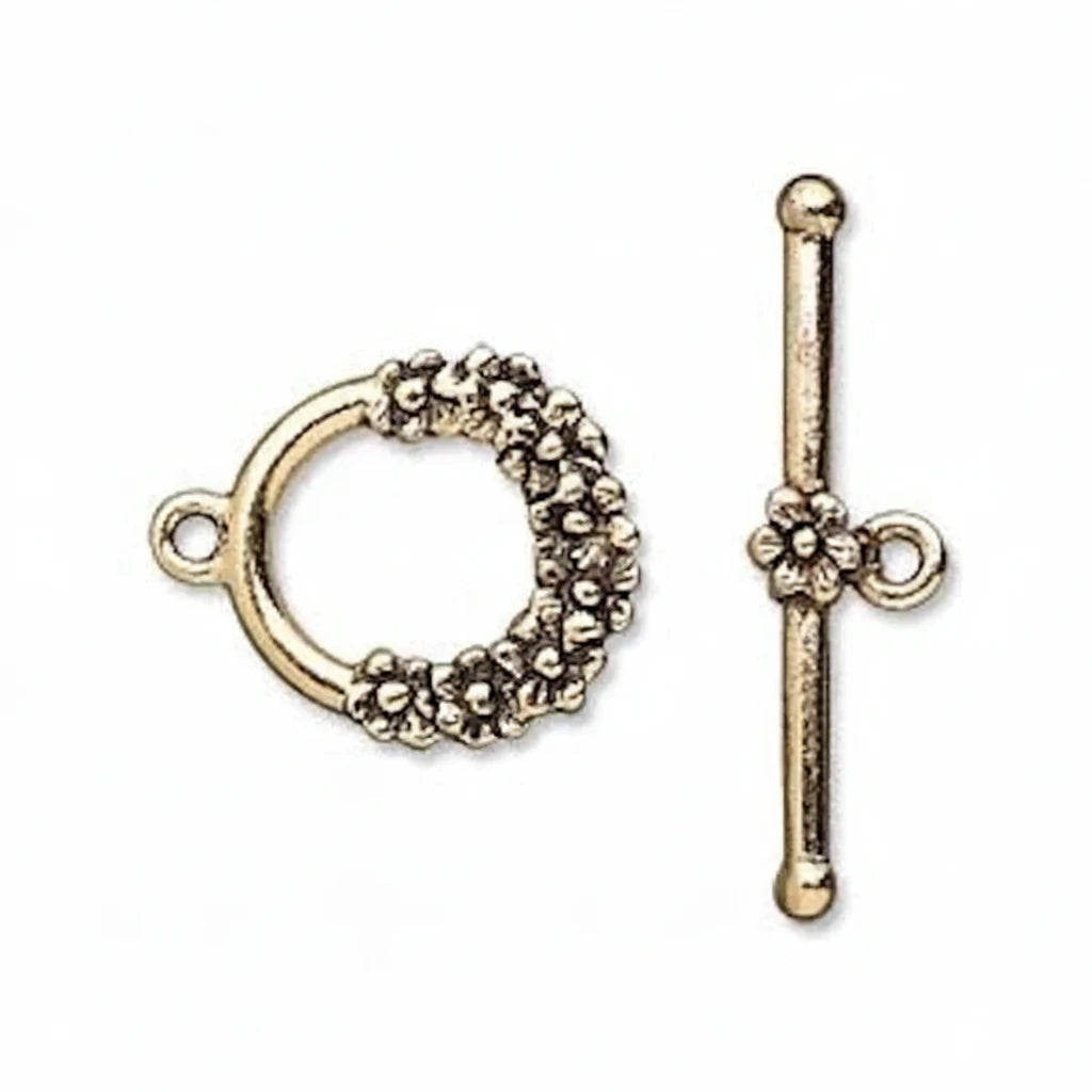 An antique gold toggle clasp set consisting of a circular ring with a textured floral border and a matching straight bar with a flower detail, shown on a plain white background.