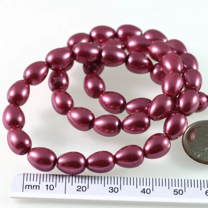 A strand of glossy, oval-shaped beads in a deep berry purple color, shown next to a US quarter coin and a millimeter ruler for scale on a white background.