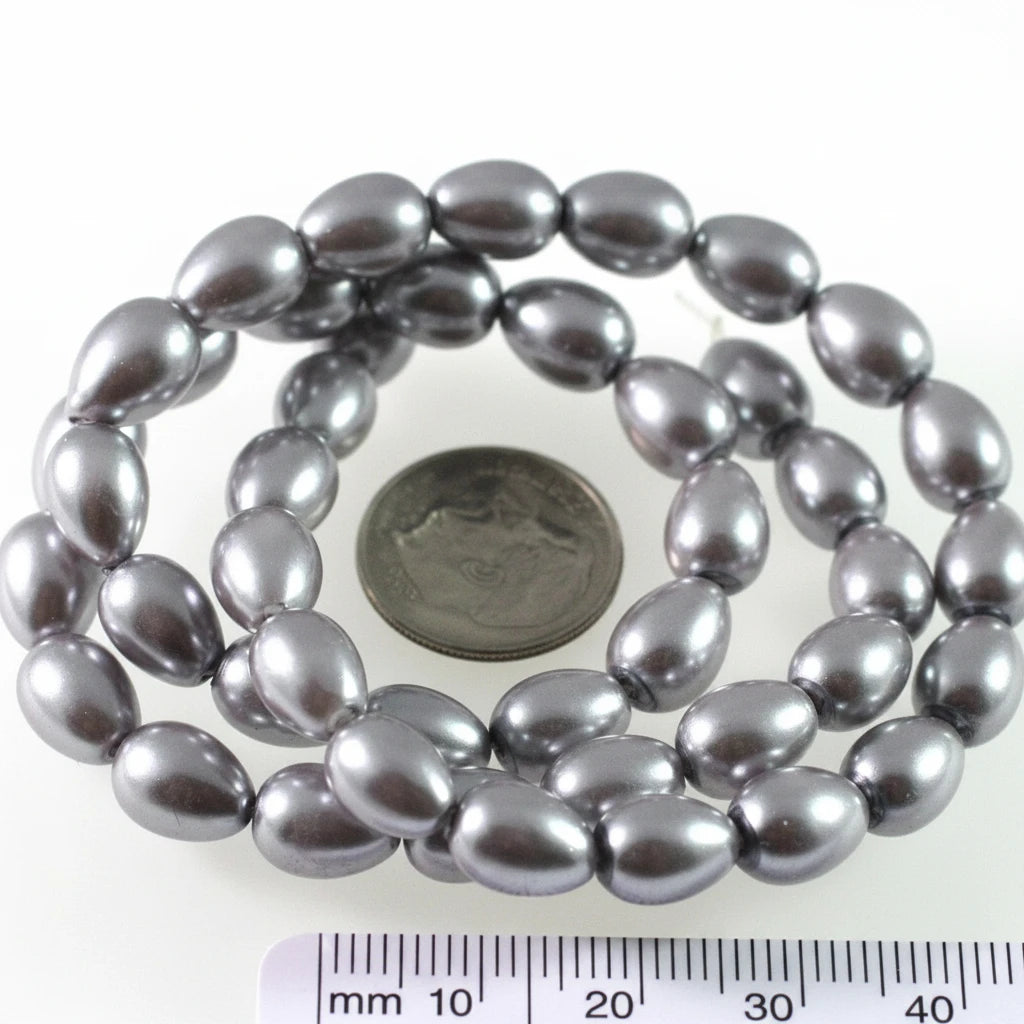 A coiled strand of dark gray teardrop-shaped beads with a metallic sheen, shown next to a US quarter coin for scale and a black measurement ruler at the bottom.