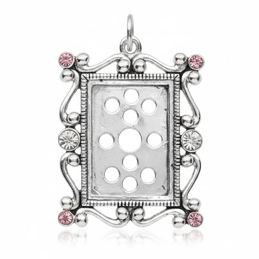 A rectangular silver pendant charm with a decorative filigree center, surrounded by a beaded scroll border adorned with small pink gemstones, shown on a solid gray background.