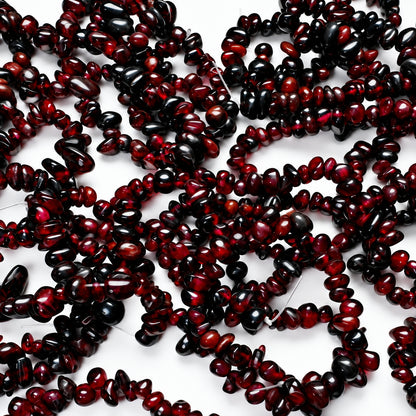 Dark red to black polished gemstone chips, likely garnet, arranged in loose strands on a white background.