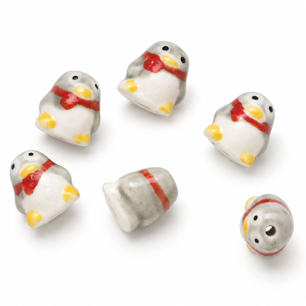Five small ceramic penguin beads shown from different angles on a plain white background. The beads are white with yellow feet and beaks, black eyes, and red scarves.