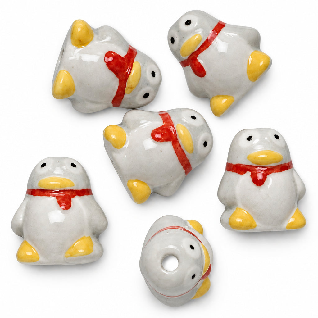 Five small penguin-shaped beads or charms on a plain white background, with one shown upside down. The beads are white with yellow feet and beaks, black eyes, and red neckties.