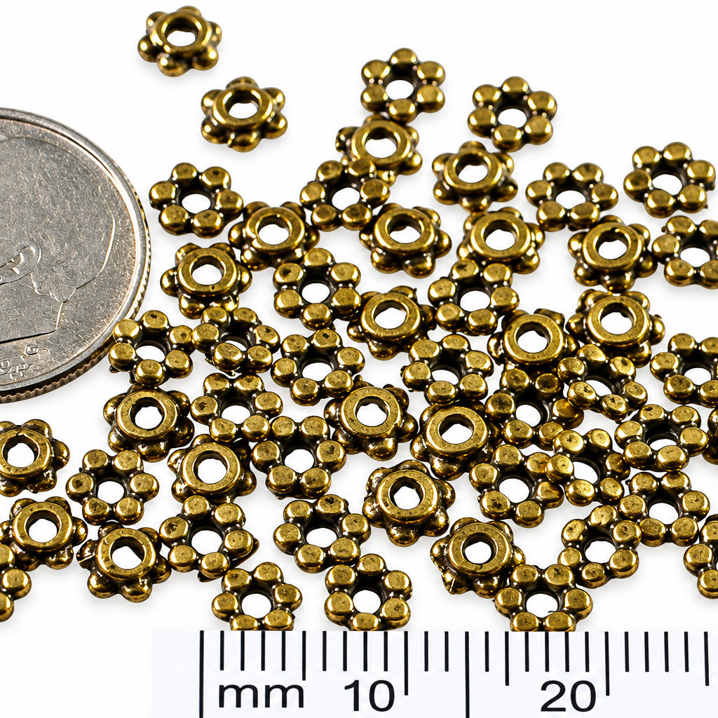 Small metallic flower-shaped findings scattered on a white background, with a coin and a millimeter ruler included for scale.