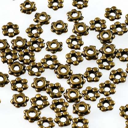 A pile of small metallic flower-shaped beads in an antique bronze finish, scattered on a plain white background.