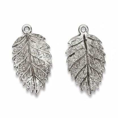 Two silver-toned leaf-shaped jewelry charms with textured engravings and top loop attachments, shown on a plain white background.
