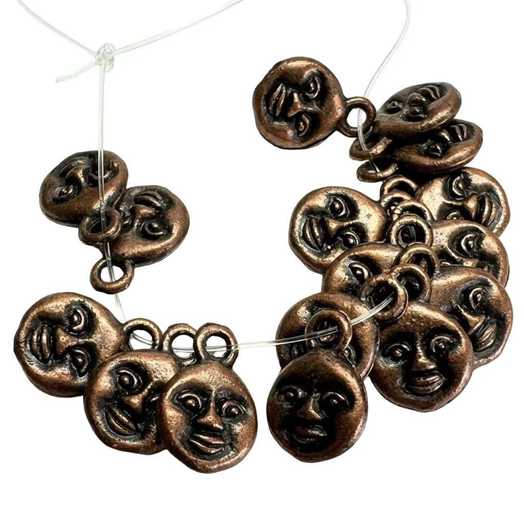 A set of bronze-colored metal jewelry charms shaped like round faces, shown on a plain white background with clear thread used for display.