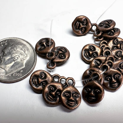 A strand of small bronze-colored metal charms shaped like stylized faces, shown on a white background next to a U.S.