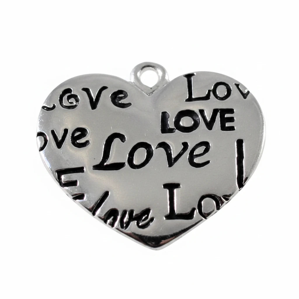 A heart-shaped silver metal charm engraved with the word 'Love' in multiple fonts, shown above a white ruler with millimeter markings for scale.