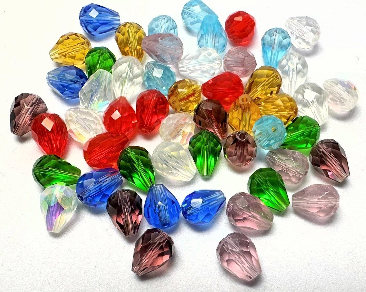 A pile of faceted glass beads in assorted colors including blue, green, red, pink, yellow, and clear, arranged on a plain white background.