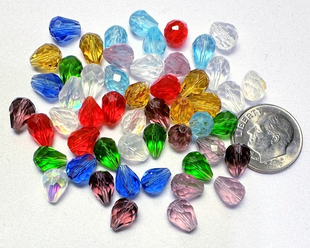 A pile of faceted teardrop-shaped craft beads in assorted colors, including blue, green, red, pink, yellow, and clear, with a U.S.