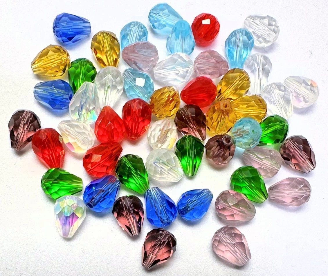 A pile of faceted crystal beads in various colors, including blue, red, green, yellow, pink, and clear, arranged on a plain white background.