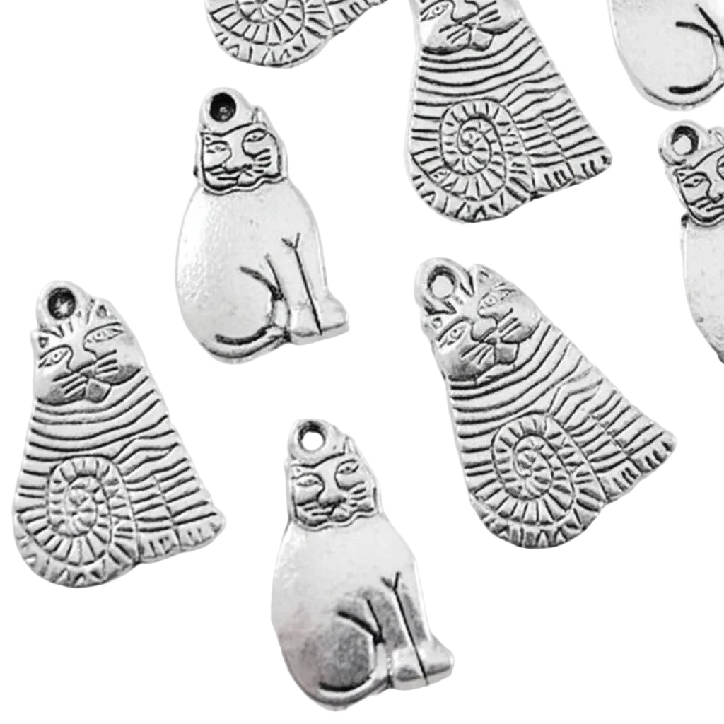 Several silver-toned metal charms shaped like stylized cats with engraved striped patterns and circular spiral details, arranged on a plain light background.
