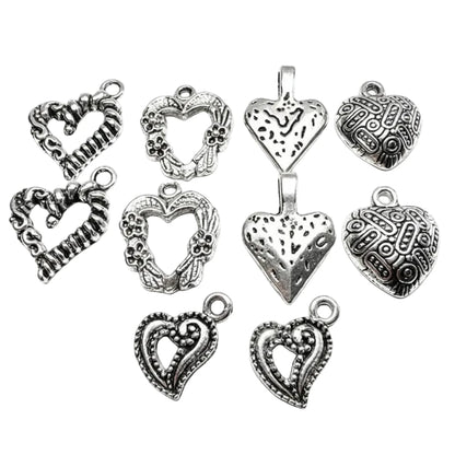 A set of nine antique silver heart-shaped jewelry charms with various textured, engraved, and filigree designs, arranged on a plain white background.