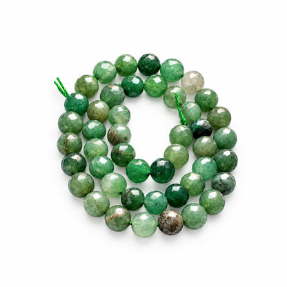 Faceted green gemstone beads strung on a cord, shown with a US quarter coin for scale on a white background.