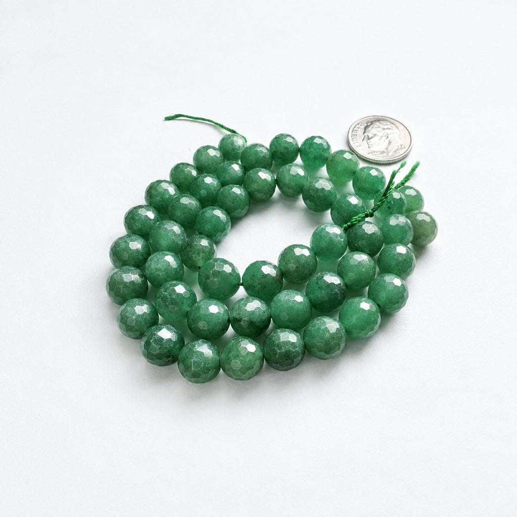 Faceted green gemstone beads on a white background with a US quarter coin for scale.